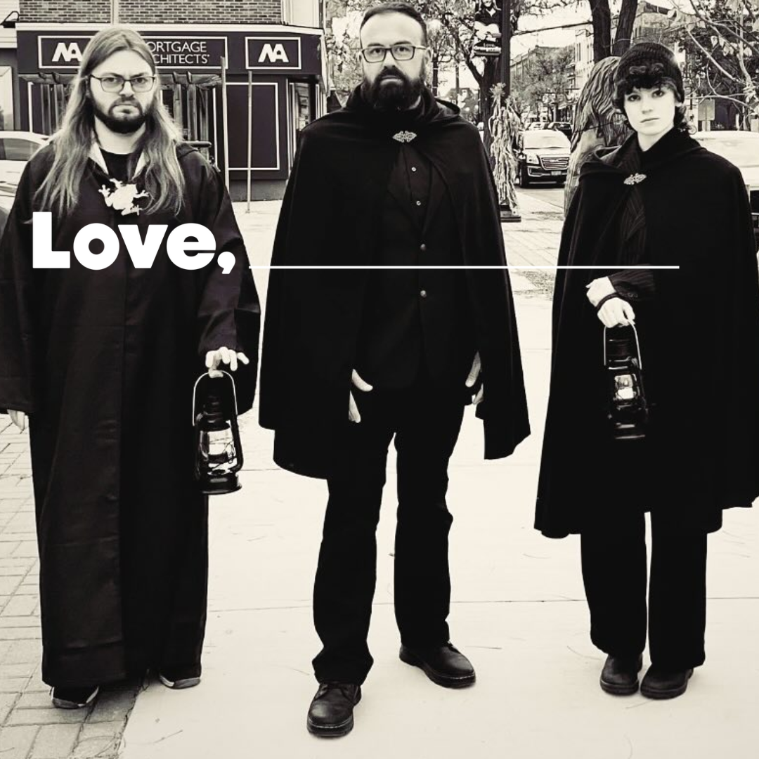 Three cloaked individuals stand on a street holding lanterns